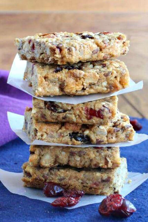 Cranberry Date Breakfast Bars are stacked sic high and divided by parchment squares every two bars. Sitting on a blue mat with a purple napkin.