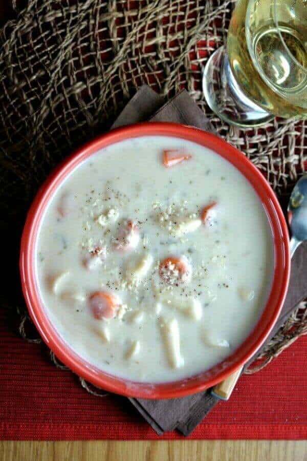 Dairy-Free Pasta Alfredo Soup is ivory colored with pasta and carrots poking through the top. A overhead photo against a blue red and chocolate colors.