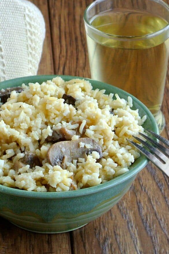 Slow Cooker Mushrooms and Rice is served in a green pottery bow' with contrasting mushrooms sticking out of the rice. Ivory cloth behind and a glass of chardonnay.