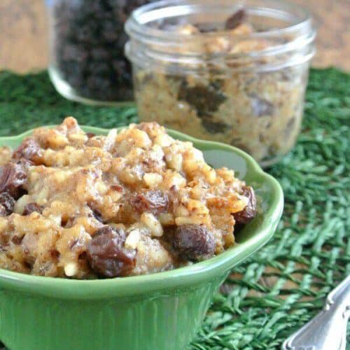 Slow Cooker Rice Pudding is in an individual green bowl and is sitting on a darker green place mat. Raisins are popping up through he golden rice pudding.
