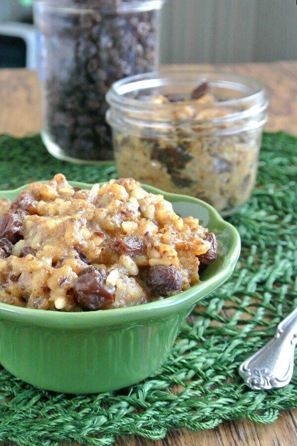 Slow Cooker Rice Pudding is in an individual green bowl and is sitting on a darker green place mat. Raisins are popping up through he golden rice pudding.