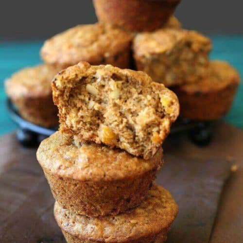 Vegan Apricot Muffins are stacked three high with a pyramid of muffins behind. The top muffin is broken in two.
