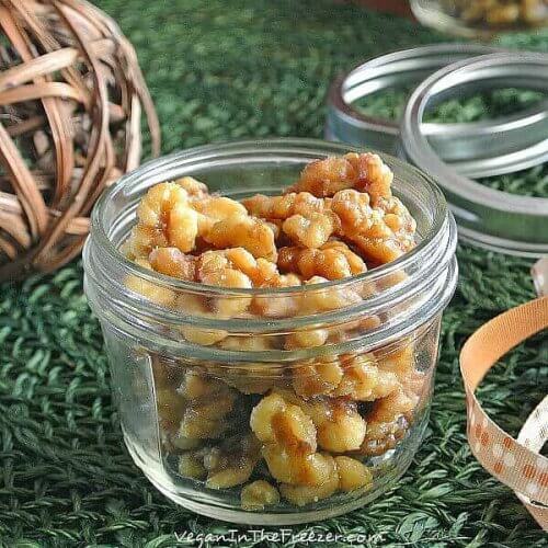 Crock pot Candied Walnuts are in a pint jar with the lid off and a festive ribbon laying the side. Lids are waiting in the background to help decorate the jars.