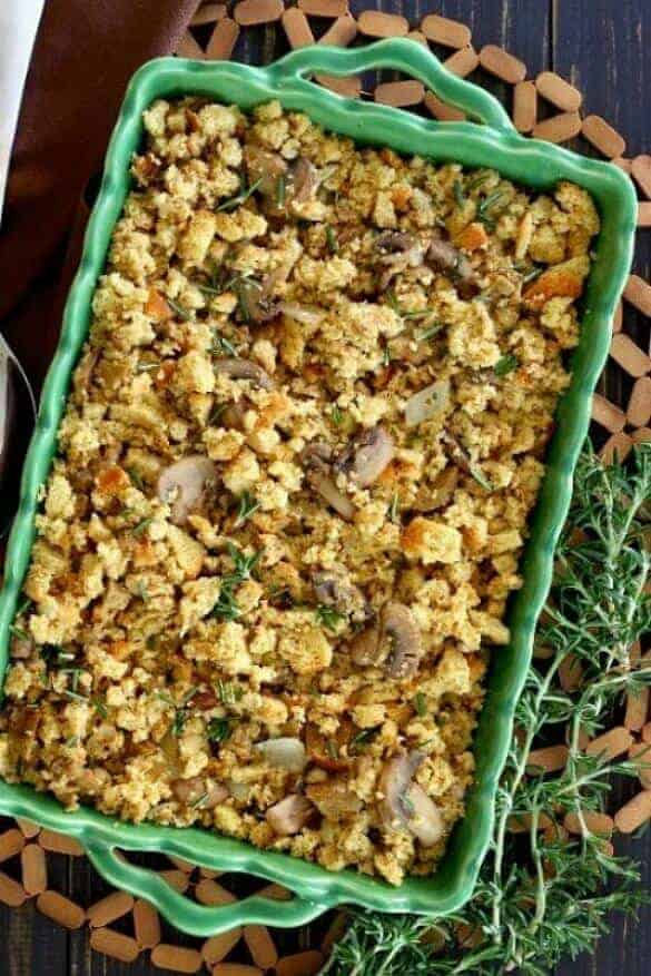 Vegan Sausage Stuffing Casserole is an above head photo and the golden stuffing is in a green casserole on a open weave wooden mat.