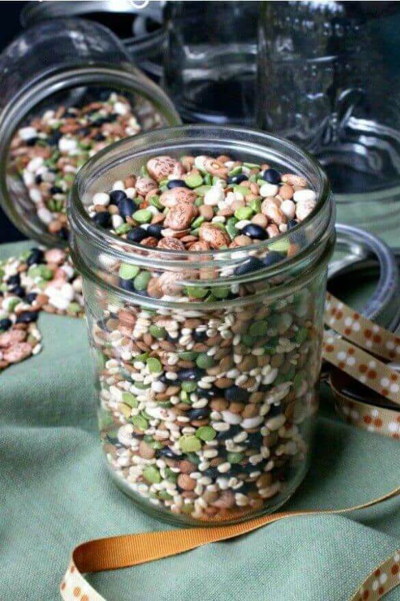 5 Legume Soup Mix with Barley is piled high in a mason jar showing all of the different bright colors. A spilled jar is behind with a cloth ribbon swirling through.