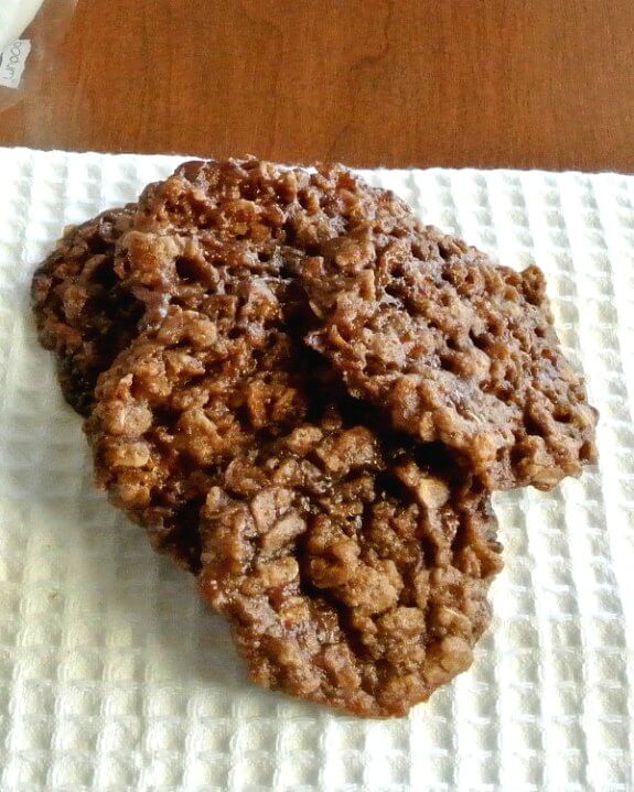 Chocolate Oatmeal Lace Cookies are spread and overlapping on a white waffle pleated cloth napkin. Titles forward to see the intricate lacy cookie pattern.