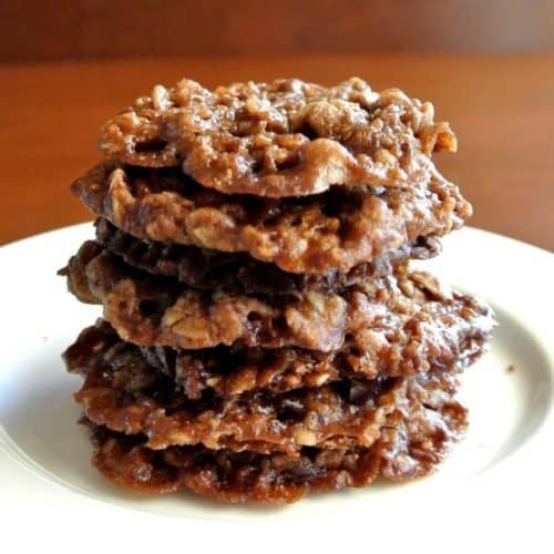Chocolate Oatmeal Lace Cookies are stacked seven cookies high in a small white plate. Tilted a bit forward to see the lacey cookie pattern