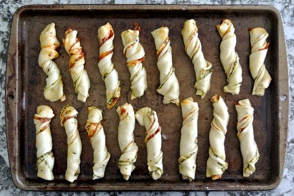 Crescent Roll Pesto Appetizers arelaying on a baking sheet. They have been prepped cut and twisted. All ready for baking.