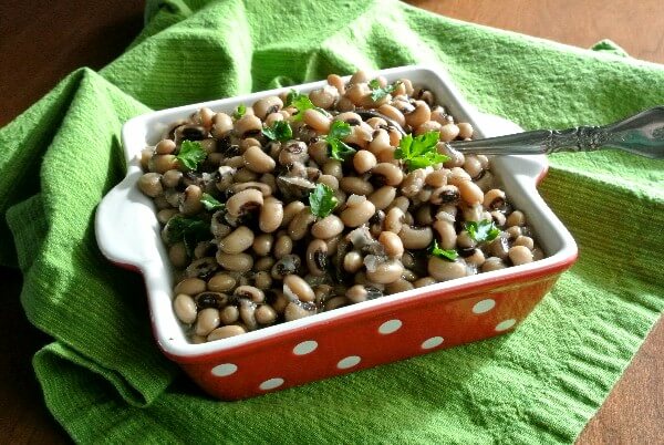 Slow Cooker Black Eyed Peas are filling a red and white polka dot bowl that's sitting on a bright green cloth. Retro festive!