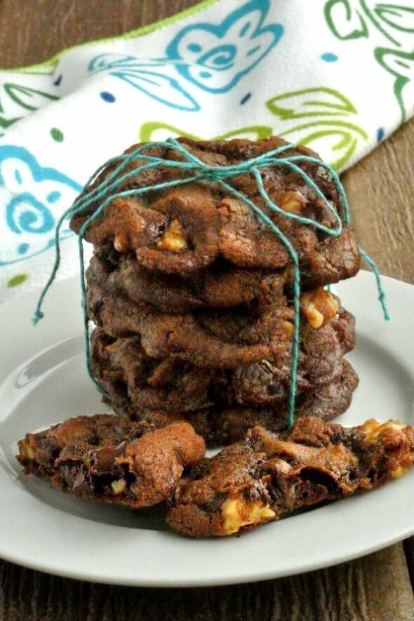 Vegan Chocolate Cookies are stacked five cookie high with a turquoise wrapping string tied in a bow on top. A broken cookie is in front on a white plate.