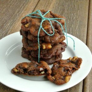 Vegan Chocolate Cookies are stacked five cookie high with a turquoise wrapping string tied in a bow on top. Walnuts showing through the chocolate.