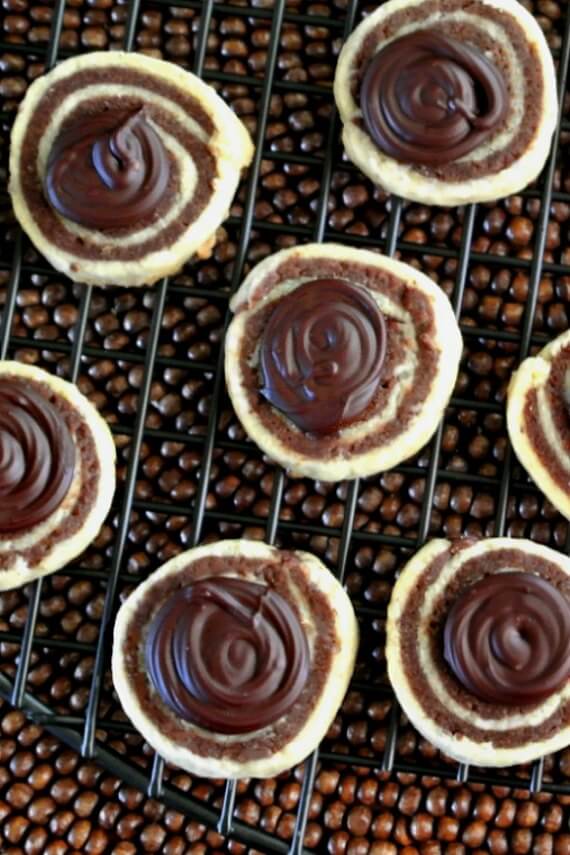 Mint Chocolate Pinwheel Cookies are an overhead photo as the cookies are resting on a black cooking rack. Swirls of chocolate have been added to the top middle tops for a more festive look.