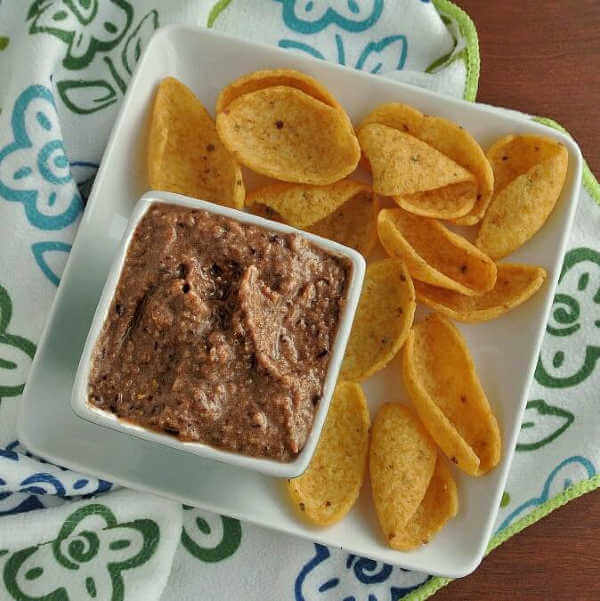 This black bean dip recipe is viewed from overhead and is on a square plate with corn chips.