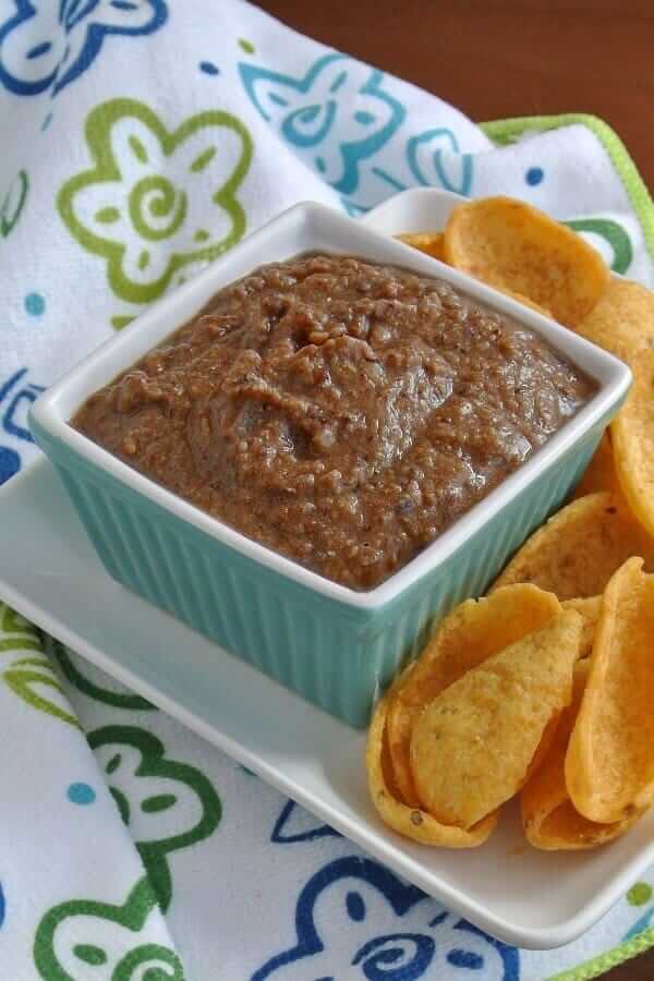 Rich black bean dip is in a square turquoise bowl and surrounded with scoops.