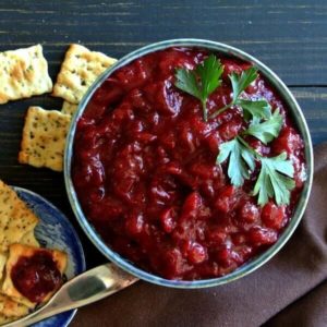Homemade cranberry sauce fills a bowl on a picnic table alongside crackers.