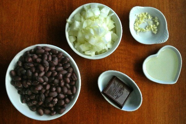 Ingredients for a special black bean dip recipe with each ingredient in a different size and shape white bowl.