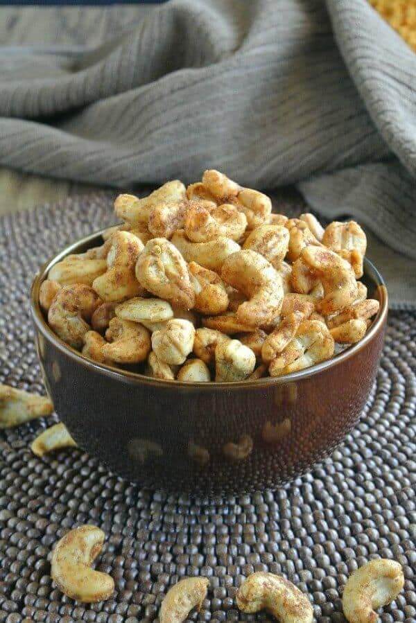 Slow Cooker Spiced Cashews are overflowing a chocolate brown bowl onto a wood beaded mat. Included in 17 Amazing Vegan Appetizers.