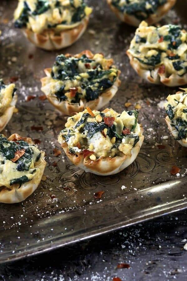 Vegan Spinach Artichoke Cups have golden brown edges and are scattered across a baking sheet.