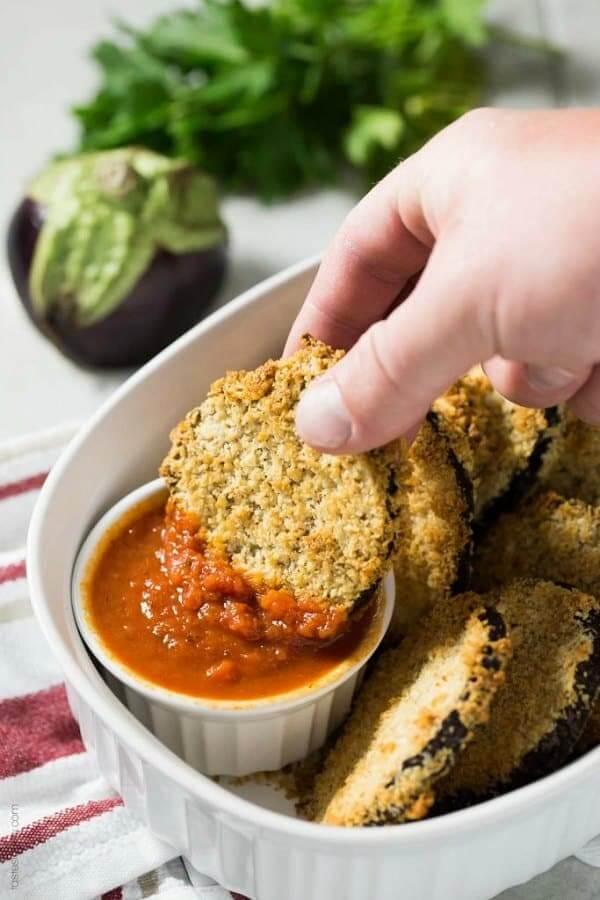 Vegan crunchy baked eggplant bites anr in a white bowl with one being dipped in a red sauce.