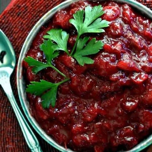 Homemade cranberry sauce fills a bowel on a red beaded mat.