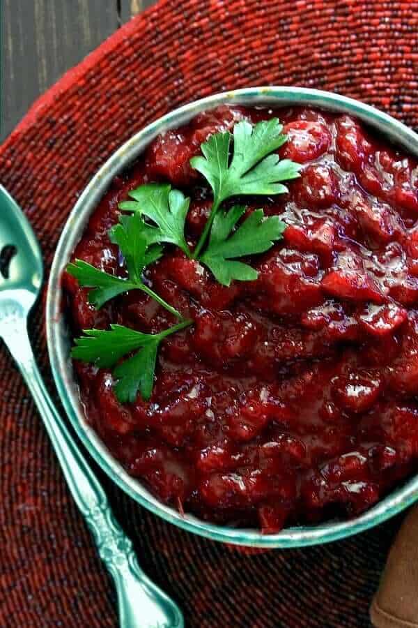 Homemade cranberry sauce fills a bowel on a red beaded mat.