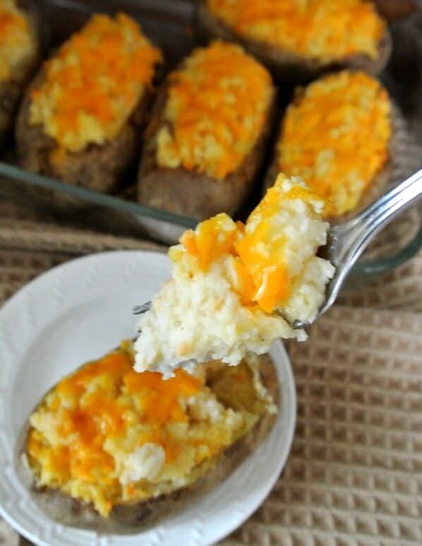 Dairy-Free twice baked potatoesはキャセロールに入れ、前皿に1つずつ載せています。 フォーク一杯が目の前にあり、クローズアップされます。