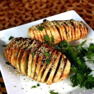 Air Fryer Hasselback Potatoes tilted toward the camera on a square plate and sprinkled with vegan Parmesan and fresh parsley.