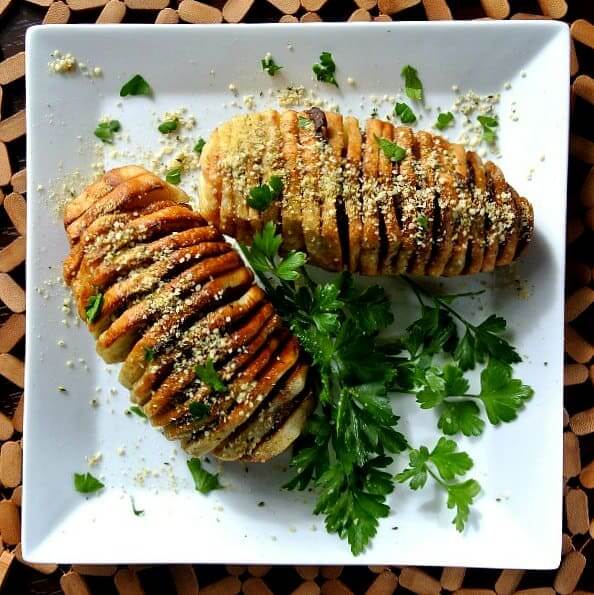 Air Fryer Hasselback Potatoes in an overhead photo on a square plate and sprinkled with vegan Parmesan and fresh parsley.