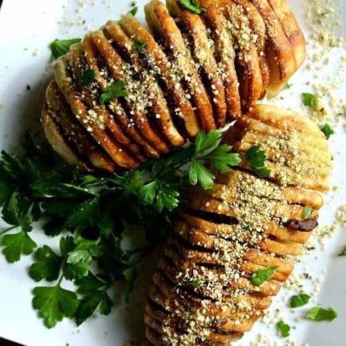Air Fryer Hasselback Potatoes in an overhead photo on a square plate and sprinkled with vegan parmesan and fresh parsley.