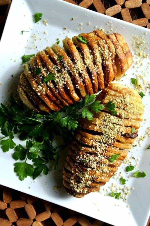 Air Fryer Hasselback Potatoes in an overhead photo on a square plate and sprinkled with vegan parmesan and fresh parsley.