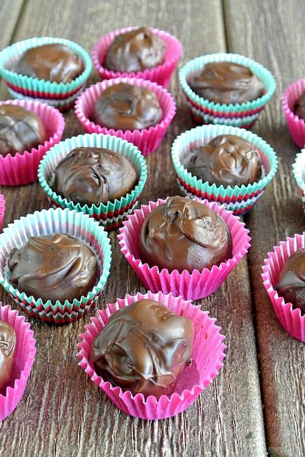 Cashew Butter Chocolate Truffles are each in their own bright pink paper cup spread across a wood topped picnic table.