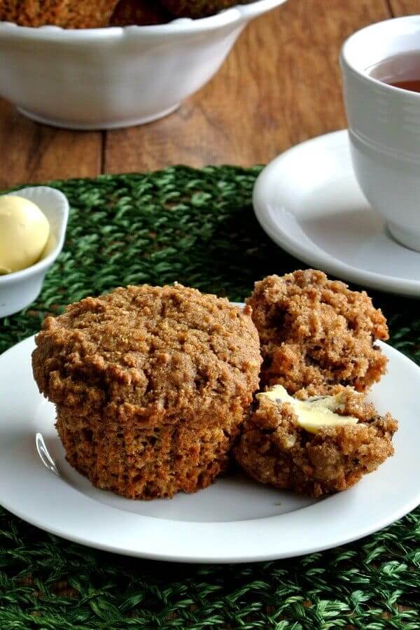 Healthy Morning Muffins are split open and buttered with dairy-free butter on a white plate and green mat. Coffee to the right.