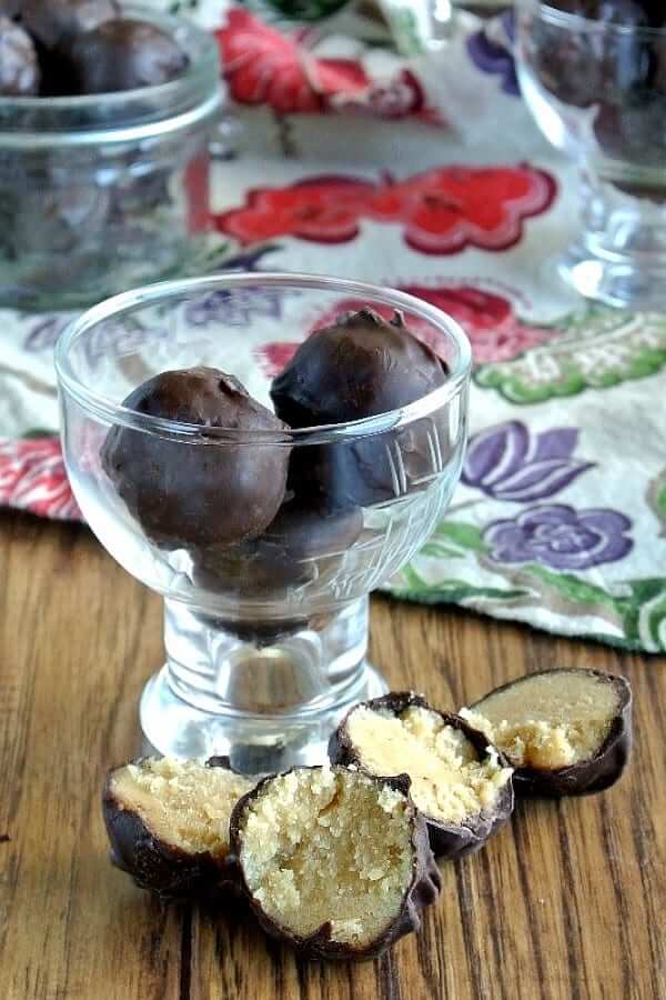 Peanut Butter Fudge Truffles are piled in a small glass container with two broken apart in front.