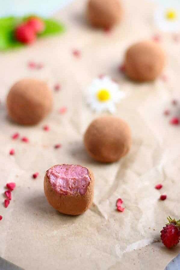 Cocoa covered Vegan Strawberry Truffles spread across parchment with strawberry bits.