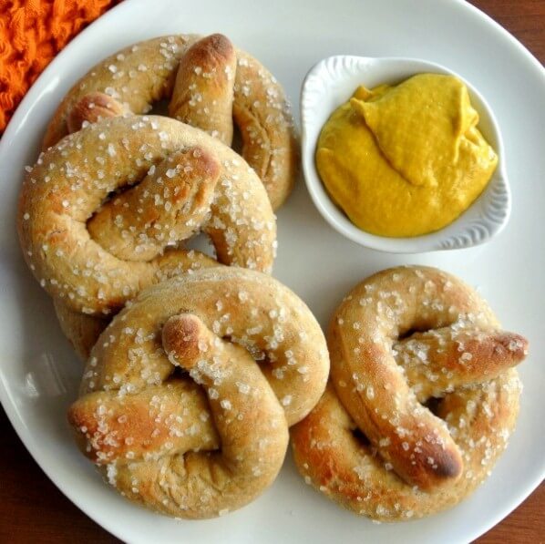 Overhead photo of three large soft pretzels sitting next to a little bowl of mustard.
