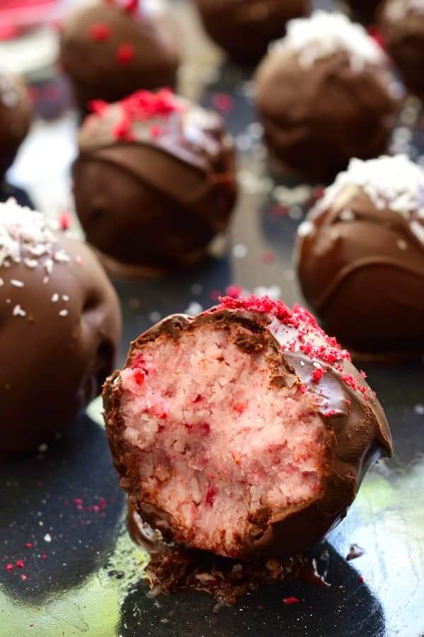 These raspberry bounty balls are scattered across a baking sheet with a bite out of the front showing a creamy raspberry filling.