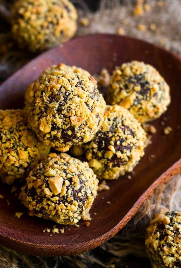 Five golden covered Snicker's Bliss Balls are piled in a wooden bowl.