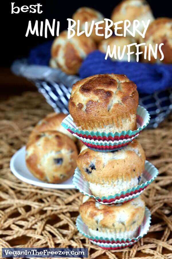 Three of the best mini blueberry muffins stacked three high on a open woven straw met with a silver basket full of more behind.