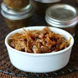 Glistening golden slow cooker caramelized onions are filling a small white bowl with half pint canning jars stacked filled and stacked behind.