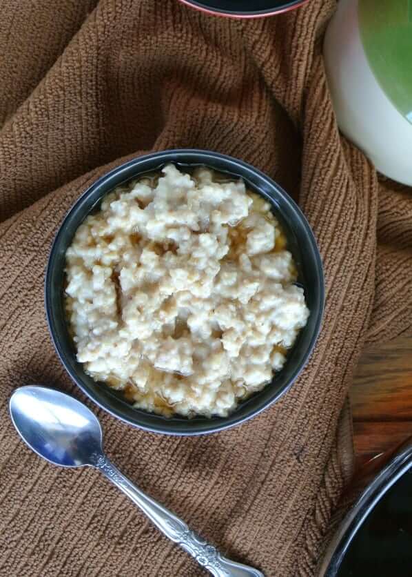 Slow Cooker Irish Oatmeal is filling a blue porcelain bowl and cropped in half with a spoon scooping up a bite.bowl in an overhead photo on a brown cloth and spoon on the side.