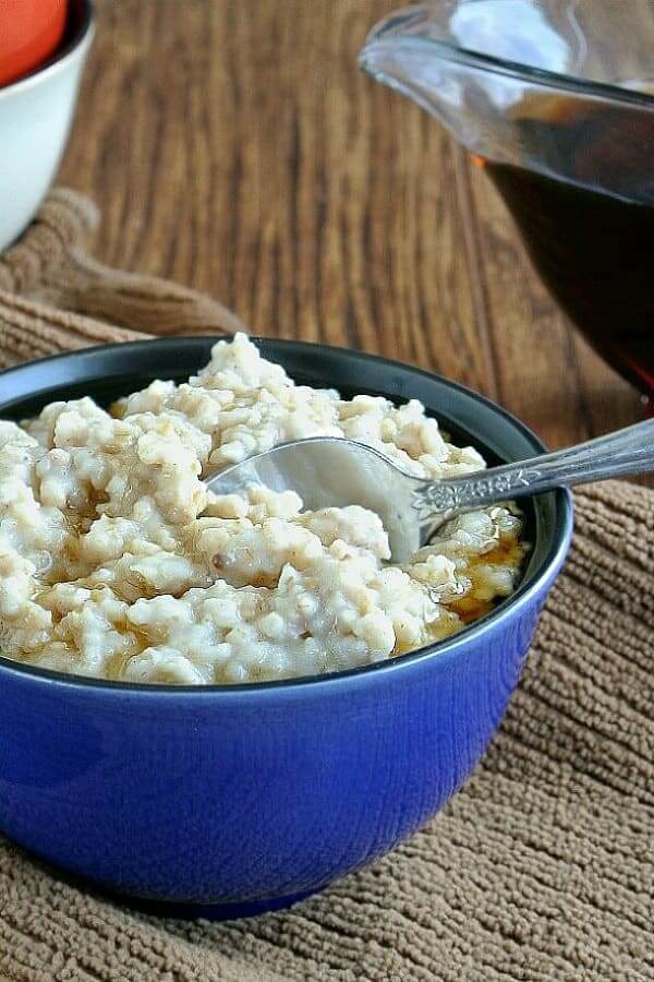 Slow Cooker Irish Oatmeal is filling a blue porcelain bowl and cropped in half with a spoon scooping up a bite.
