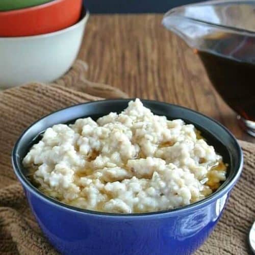 Slow Cooker Irish Oatmeal is filling a blue porcelain bowl with maple syrup floating on top.