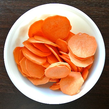 Air Fryer Sweet Potato Chips are photographed from above with a bowl filled with thin slices of raw sweet potatoes.