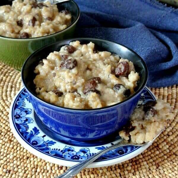 Straight on view of a cropped blue bowl full of creamy old fashioned rice pudding with a spoonful on the side.