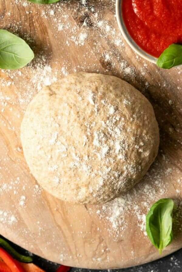 Overhead view of a perfectly round ball of pizza dough on a cutting board with flour.