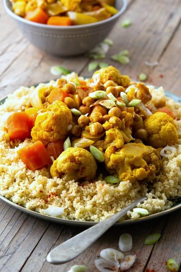 Front view of couscous topped North African food containing cauliflower, carrots, chickpeas and spices.