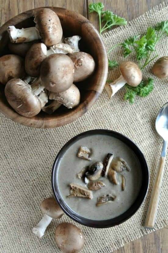 Overhead photo of a bowl of richly colored wild mushroom soup and a bowl of fresh mushrooms.