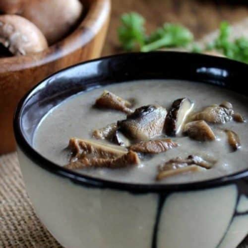 An Asian designed bowl is cropped for the photo and full of creamy mushrooms soup with extra wild mushrooms on top.