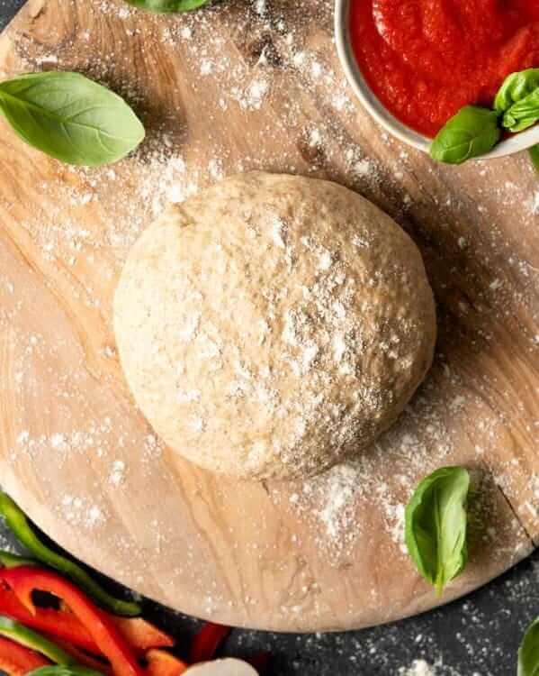 An overhead photo of a smooth ball of pizza dough on a wooden cutting board.