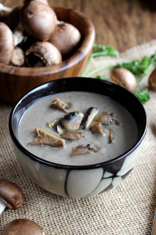 An Asian designed bowl is centered and full of creamy mushrooms soup with extra wild mushrooms on top.